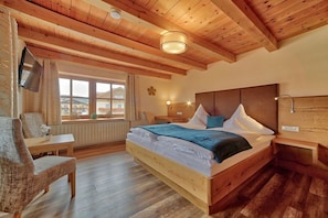 A bedroom with a wooden bed, a chair, a TV, and a window with a view. - Holiday home with 2 bedrooms (Zachenberg)