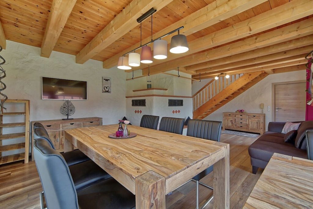 Un comedor amplio con una larga mesa de madera, varias sillas y una escalera que lleva a un nivel superior.
