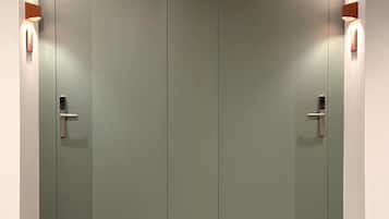 A pair of closed doors with a light switch on each, a wall-mounted light fixture on the left, and a wall-mounted light fixture on the right.