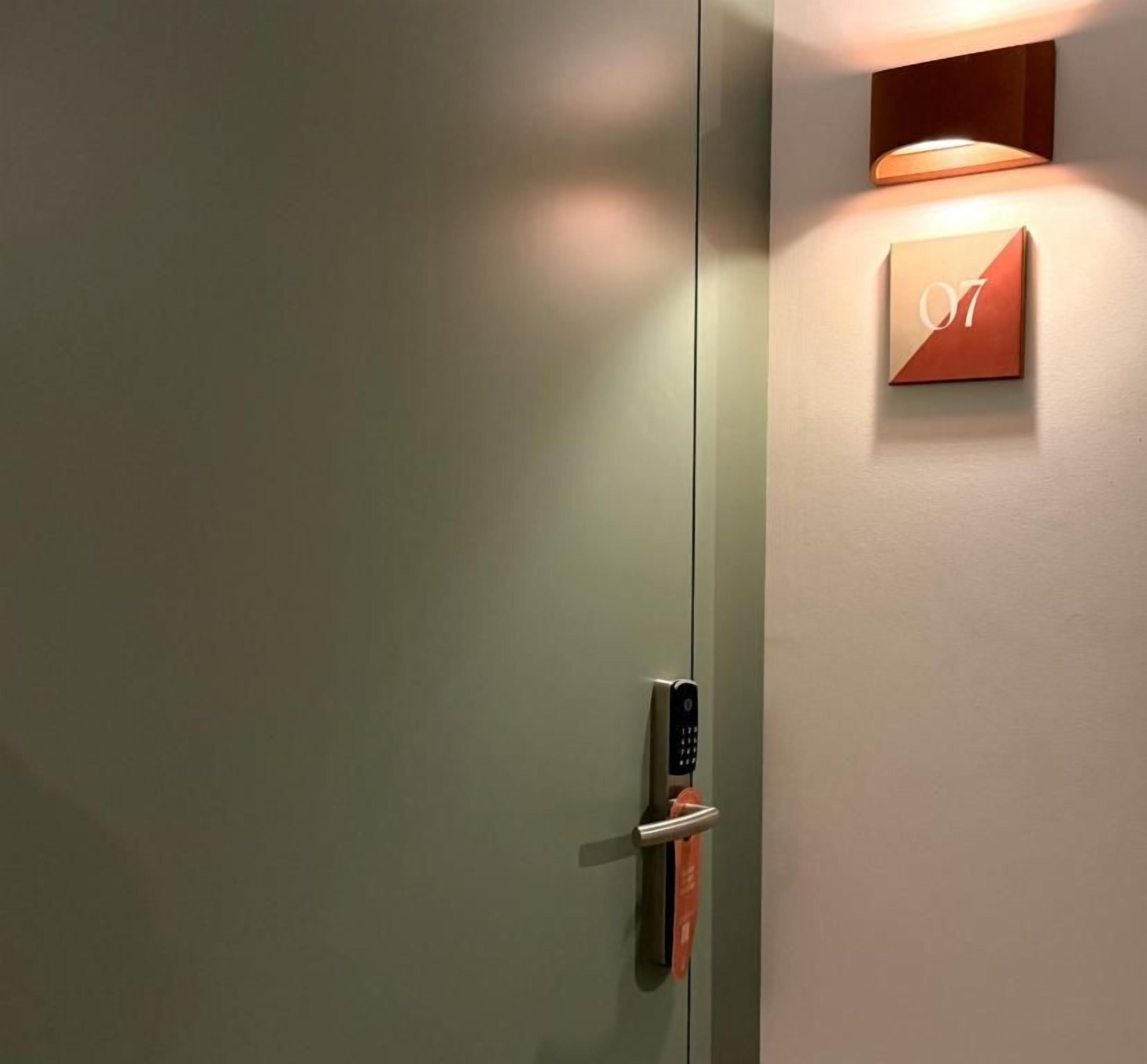 Eine Hotelzimmertür mit Kartenlesegerät und einer an der Wand montierten Nummernschild, das die Zimmernummer 07 anzeigt.