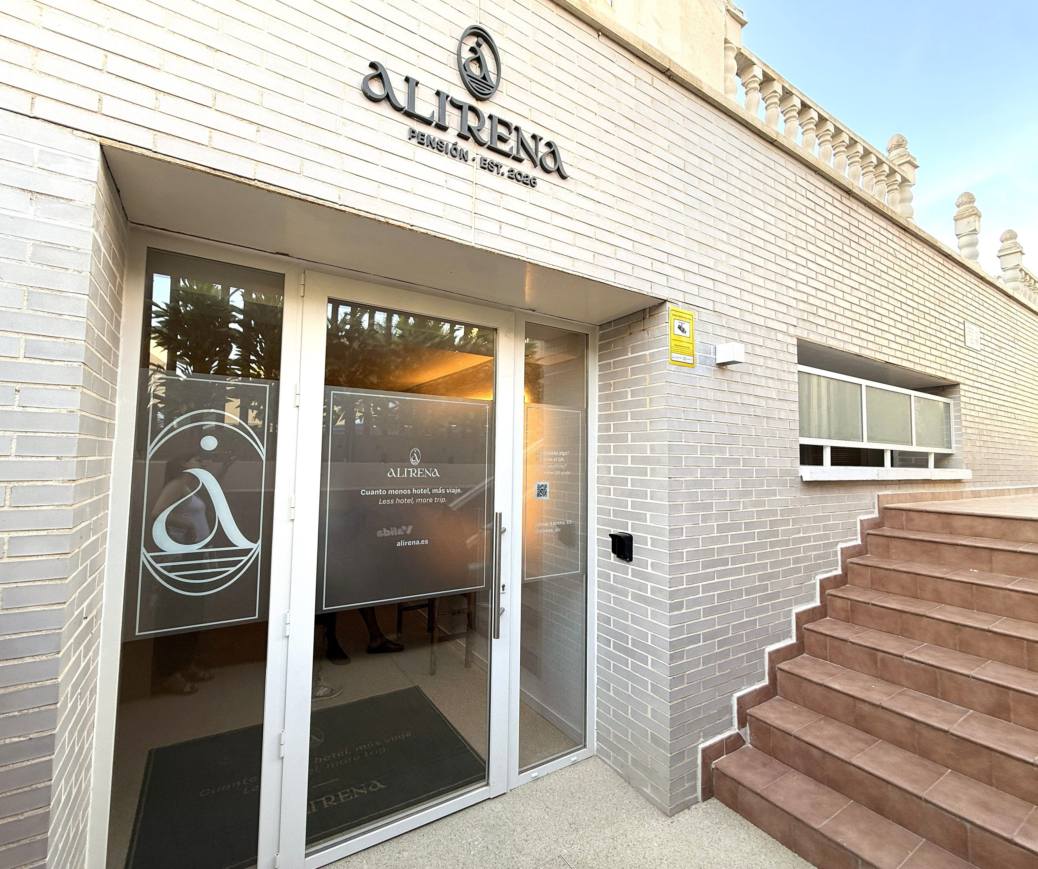 Entrada de un hotel con puerta de cristal, un cartel sobre la puerta y una escalera que conduce a la entrada.