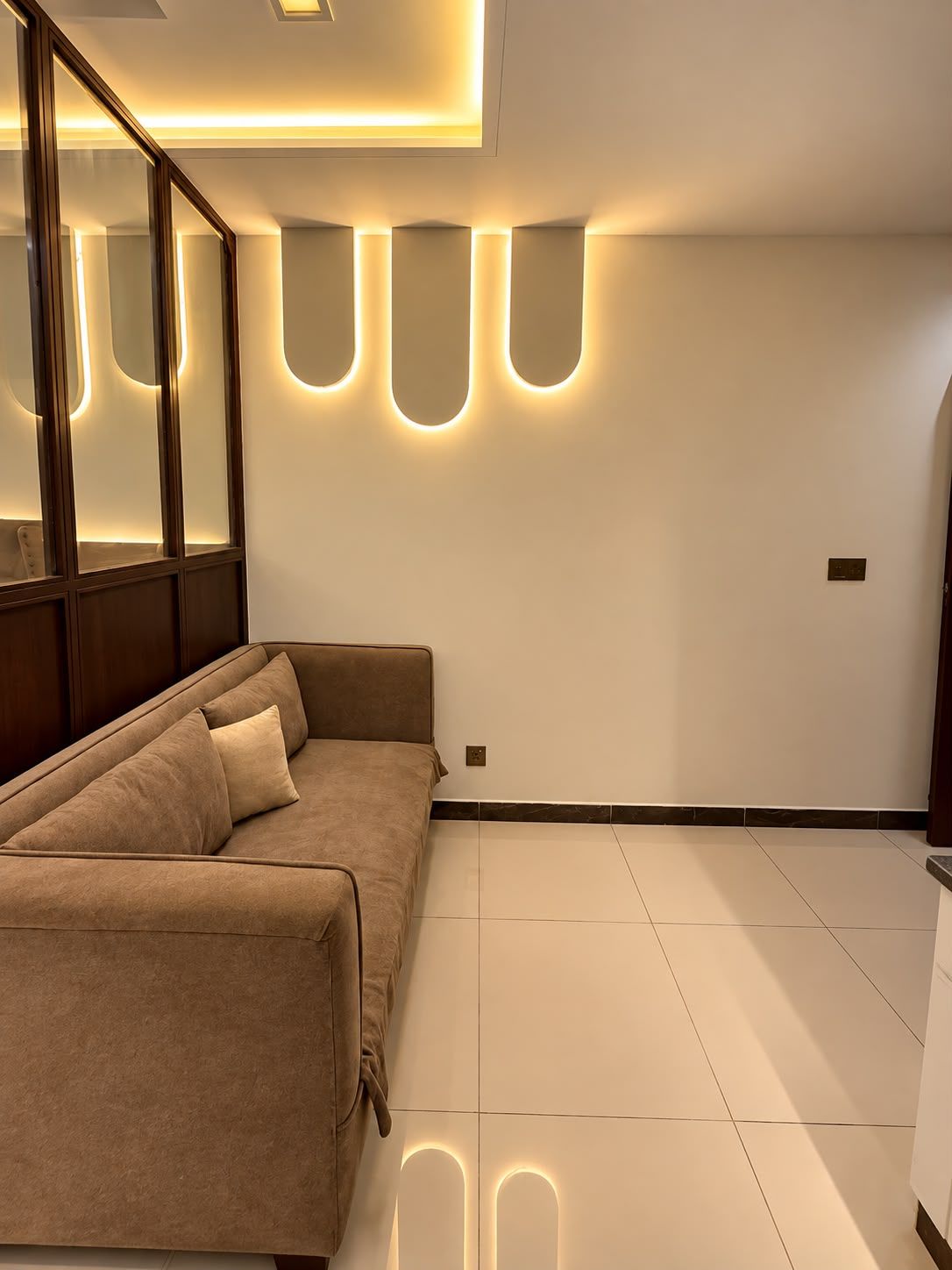 Un salon moderne avec un canapé d’angle, un éclairage encastré et un grand miroir.