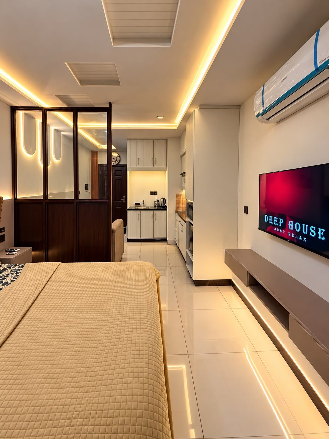 Ein modernes Hotelzimmer mit Bett, Fernseher, Küchenzeile und einer Schiebetür zum Badezimmer.