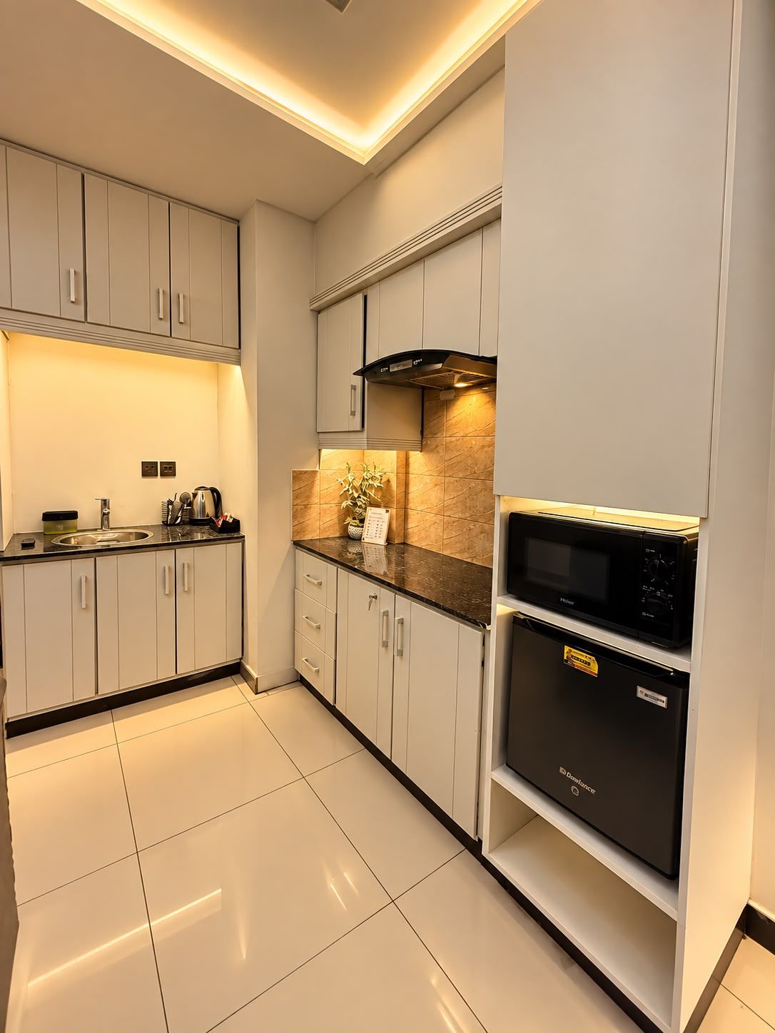 A modern kitchen with white cabinets, a black microwave, and a stainless steel sink.