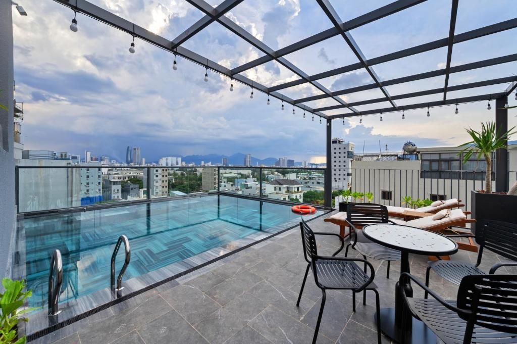A rooftop pool area with a glass barrier, lounge chairs, and a table.