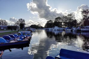 A marina with boats docked along the water's edge, a building on the left, and trees in the background. - Anita Beitelmann at the Timmeler-Meer (Großefehn - Timmel)