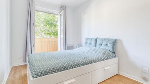 A bedroom with a bed, a window with curtains, a radiator, and a wooden floor. - Quiet one-bedroom apartment with a large balcony and free parking (Oullins)