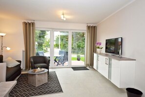 A modern living room with a sofa, armchair, coffee table, and a television on a cabinet. - Holiday apartment with 2 bedrooms (Norddeich)
