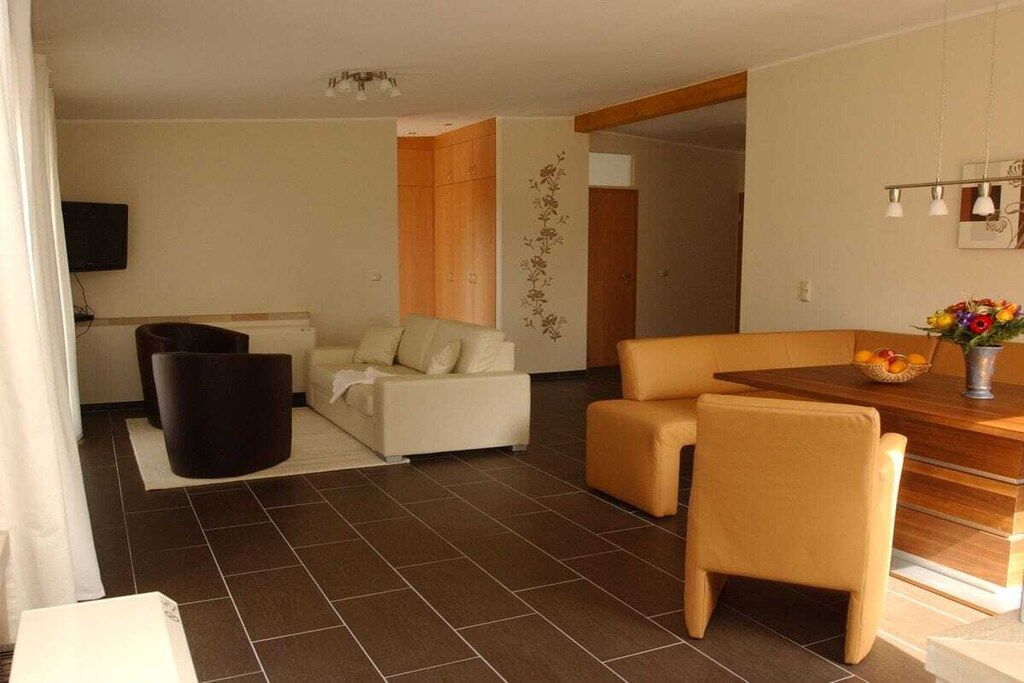 A modern living room with a sofa, armchair, and a dining table with chairs.