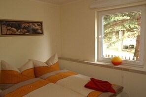 Ein Schlafzimmer mit Bett, Kissen, einem Fenster mit Blick auf Bäume und einem Bild an der Wand.