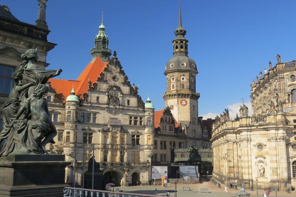 A historic building with ornate architecture, a prominent clock tower, and a statue in the foreground.