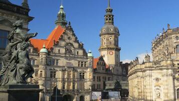 A historic building with ornate architecture, a prominent clock tower, and a statue in the foreground.
