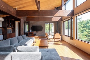 Uma sala de estar moderna com um sofá seccional grande, uma televisão de tela plana presa a uma parede de pedra e uma mesa de jantar de madeira com cadeiras.