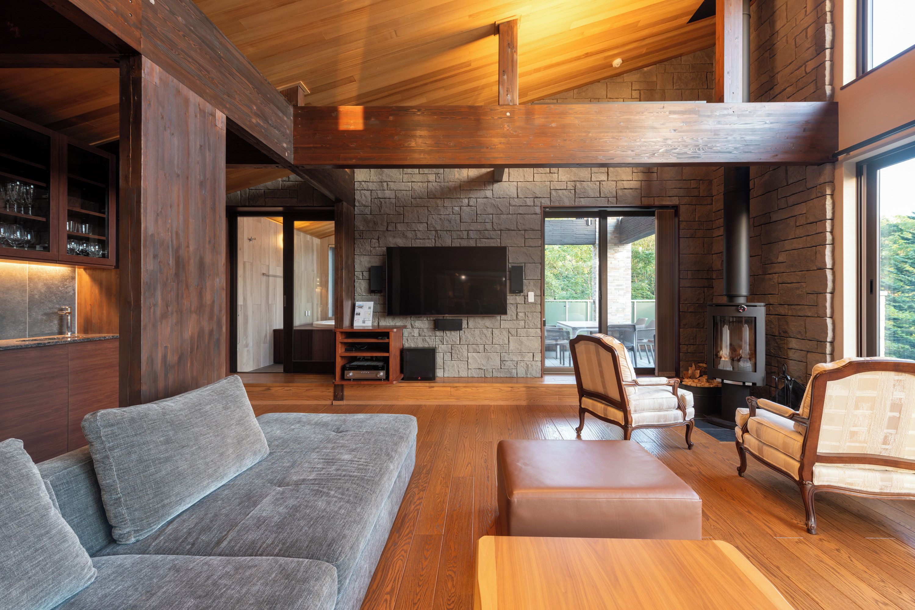 A spacious living area with a stone fireplace, wooden ceiling beams, and a large flat-screen TV mounted on the wall.