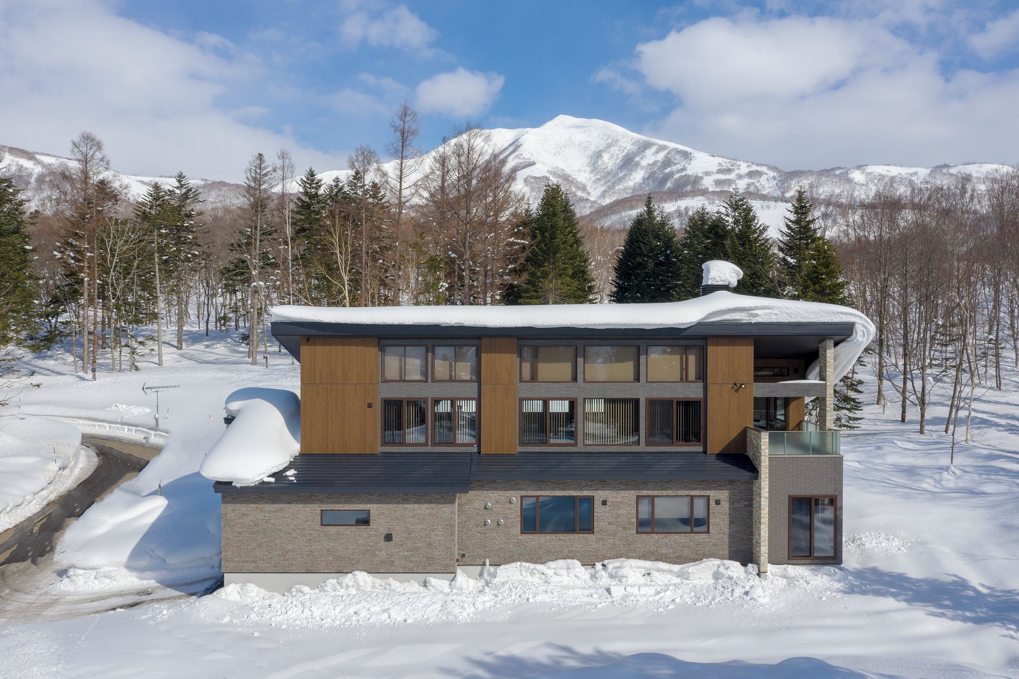 Um edifício moderno de dois andares com telhado coberto de neve, rodeado por uma paisagem nevada e árvores.