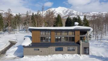 Um edifício moderno de dois andares com telhado coberto de neve, rodeado por uma paisagem nevada e árvores.