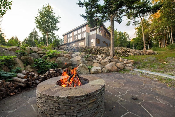 A stone fire pit surrounded by a stone wall, with a modern building in the background.