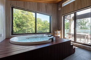 Un área de spa con un jacuzzi, suelo de madera y ventanas amplias que ofrecen vistas a árboles.