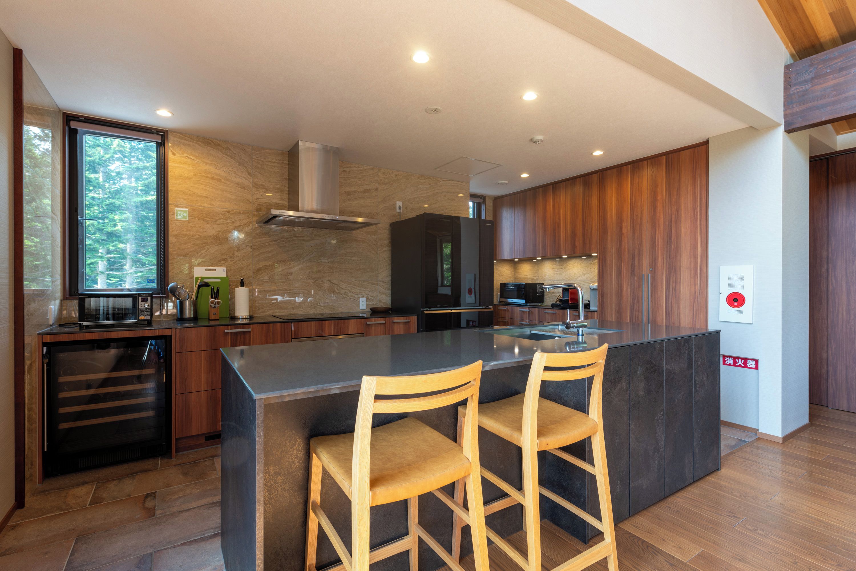 Cozinha moderna com ilha central, banquetas de madeira e eletrodomésticos embutidos.