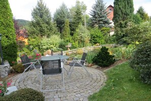 A circular patio with a table and chairs, surrounded by a garden with various plants and trees. - Holiday apartment with 2 bedrooms (Sebnitz)