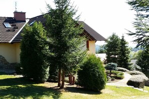 A house with a sloped roof, a stone wall, and a well-maintained garden with various trees and shrubs. - with indoor pool and sauna (Jilemnice Benecko)