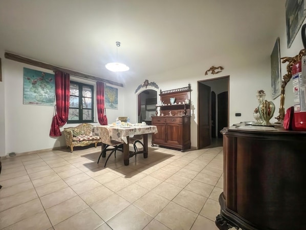 A dining area with a table and chairs, a sofa, a cabinet, and a large window with curtains.