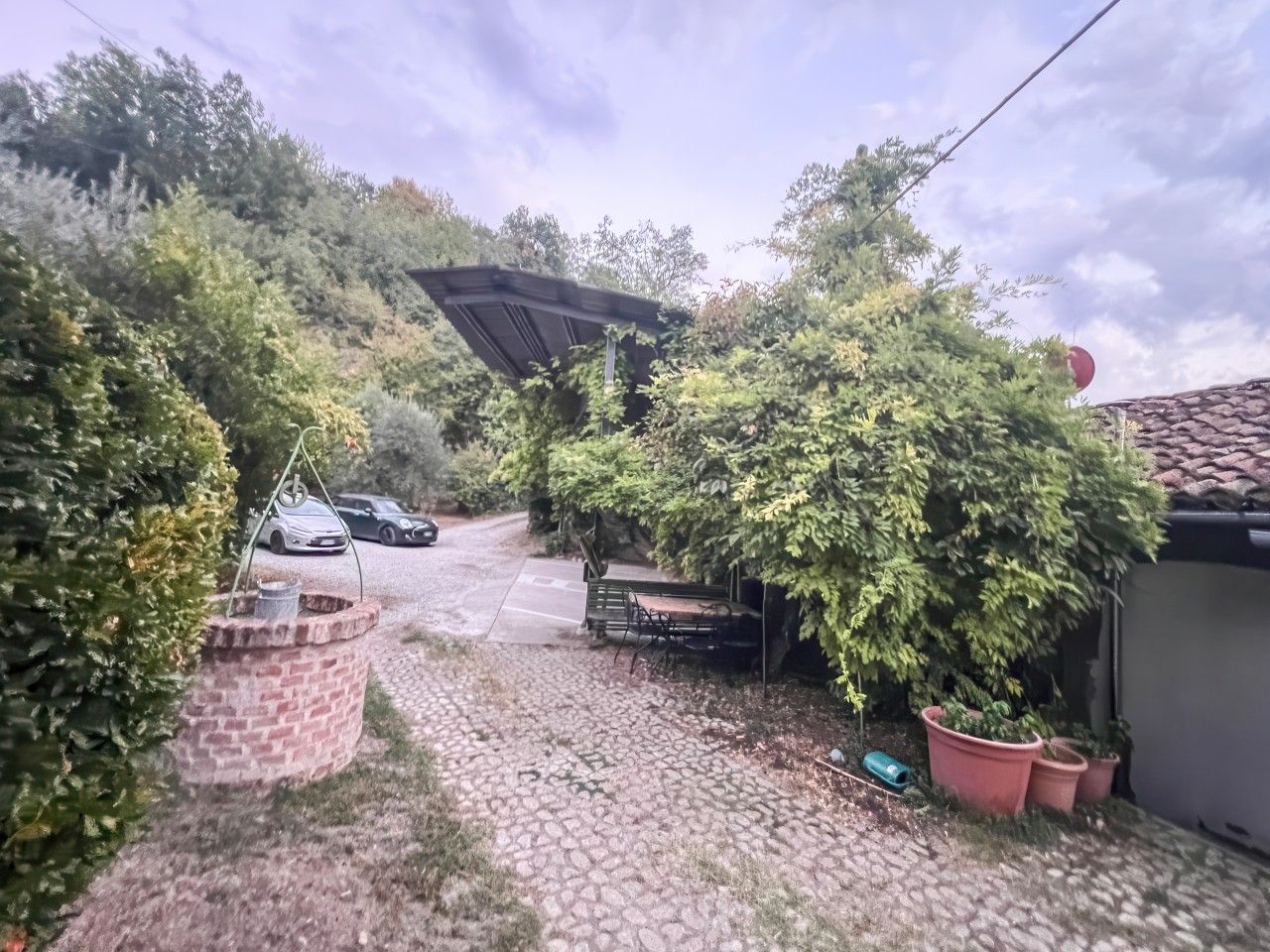 A paved pathway leading to a covered area with a bench and potted plants.