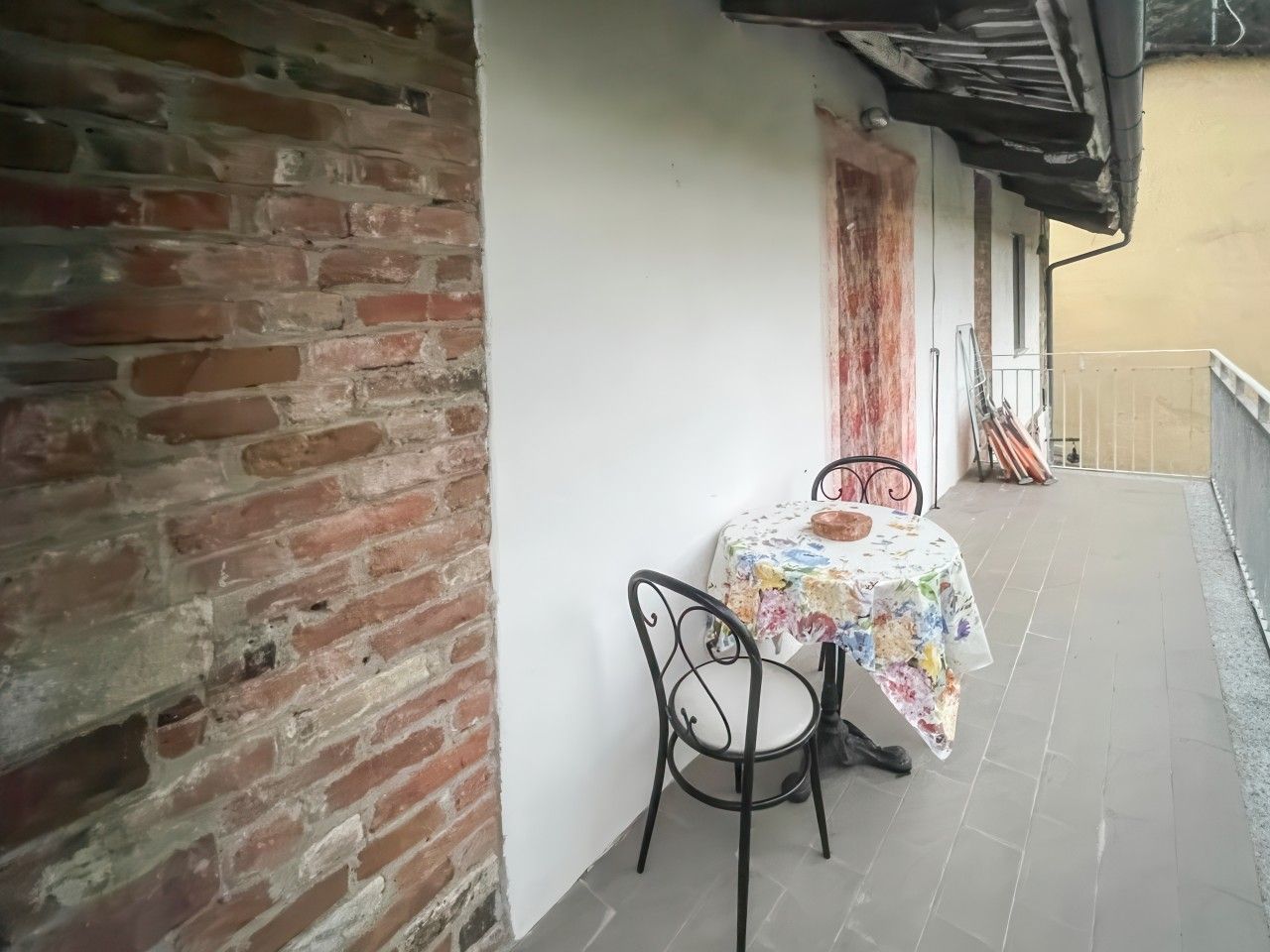 Ein Balkon mit Tisch und Stühlen, eine Ziegelwand und ein Fliesenboden.