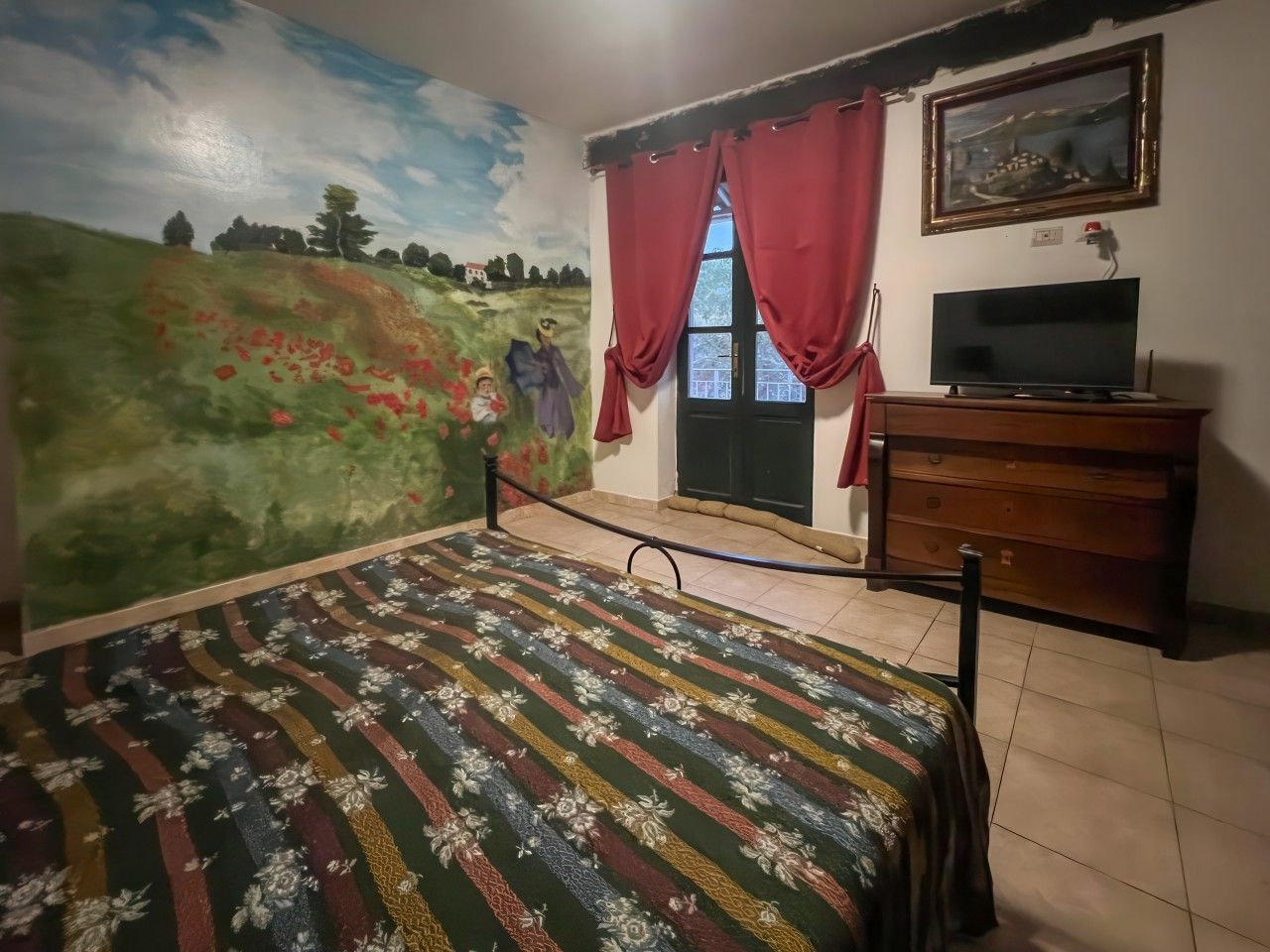 Ein Schlafzimmer mit einem Bett, einer Kommode, einem Fernseher und einem Wandgemälde.