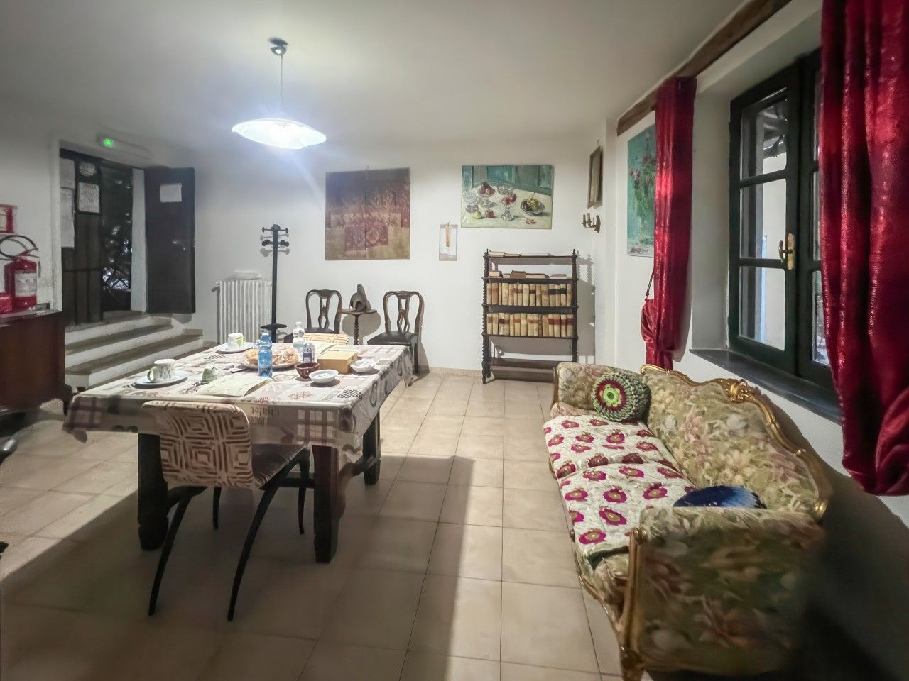 A dining area with a table set for four, a sofa with floral upholstery, and a bookshelf with books.