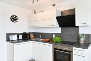A modern kitchen with white cabinets, a black countertop, a built-in oven, and a wall-mounted clock. - C in the holiday home TraumBlick (Lindau)