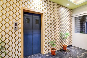 Een lift met een digitaal scherm, een behang met patroon en potplanten.