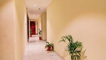 A hallway with marble flooring, potted plants, and a red door at the end.