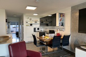 A modern kitchen with a dining area, equipped with a microwave, kettle, and various kitchen appliances. - Strandhuus Norderney (Norderney)