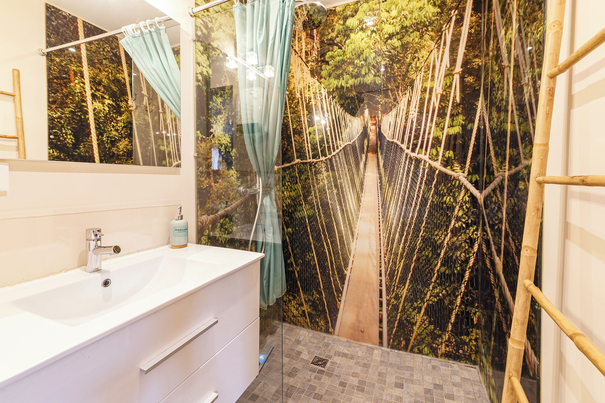 A bathroom with a white sink, a mirror, and a shower area with a rope bridge.