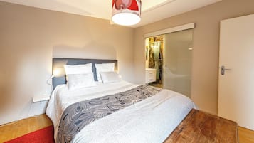 A modern bedroom with a bed, bedside tables, a nightstand, a red carpet, and a wooden floor.