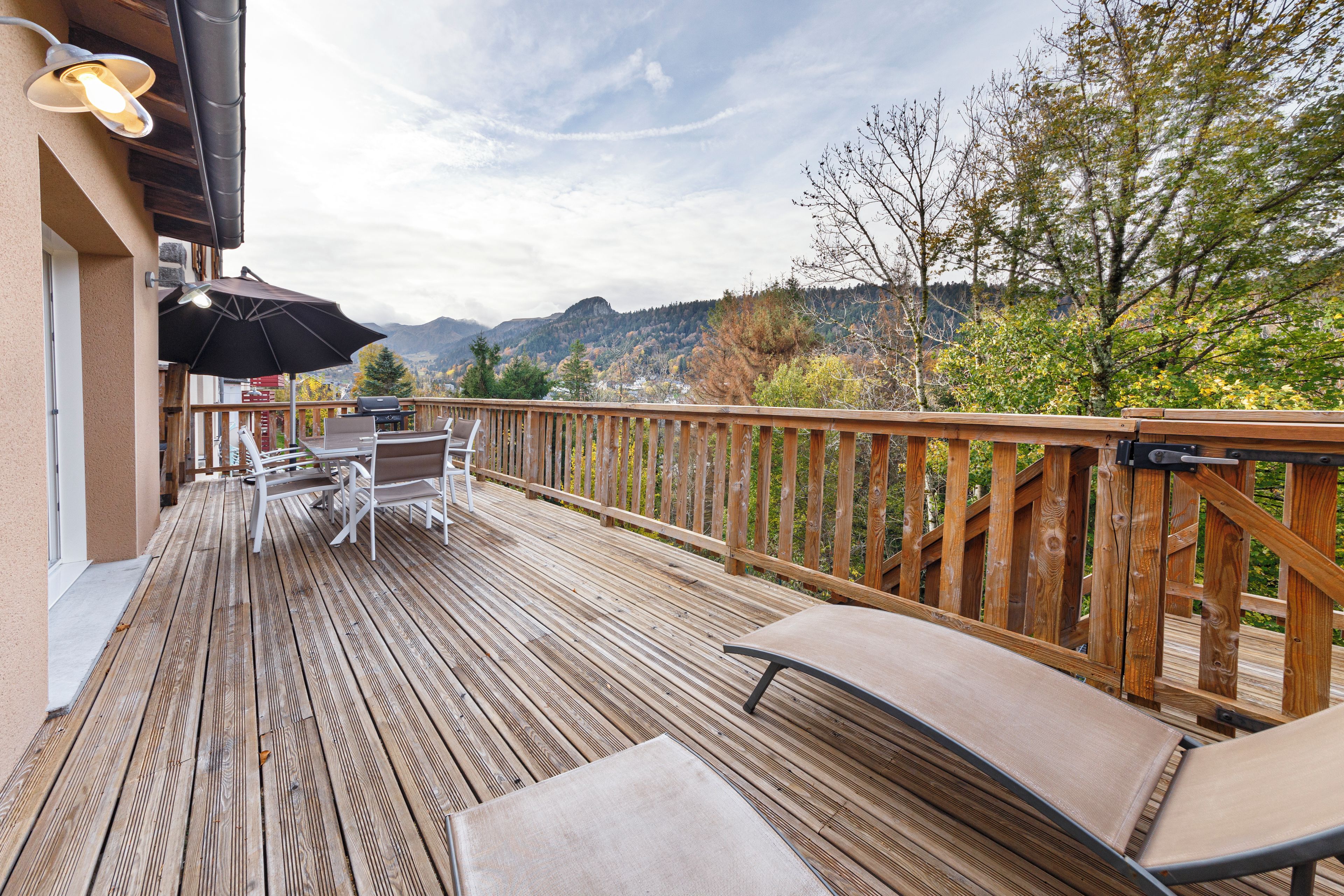 Une terrasse en bois avec des meubles d’extérieur, un barbecue et une vue sur les montagnes.