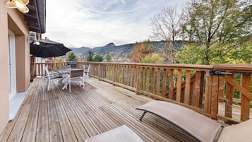 A wooden deck with outdoor furniture, a grill, and a view of mountains.