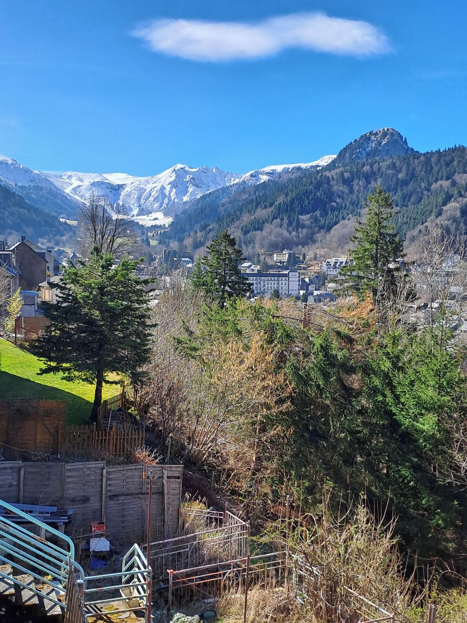 A mountainous landscape with snow-capped peaks, a town in the valley, and a clear blue sky.