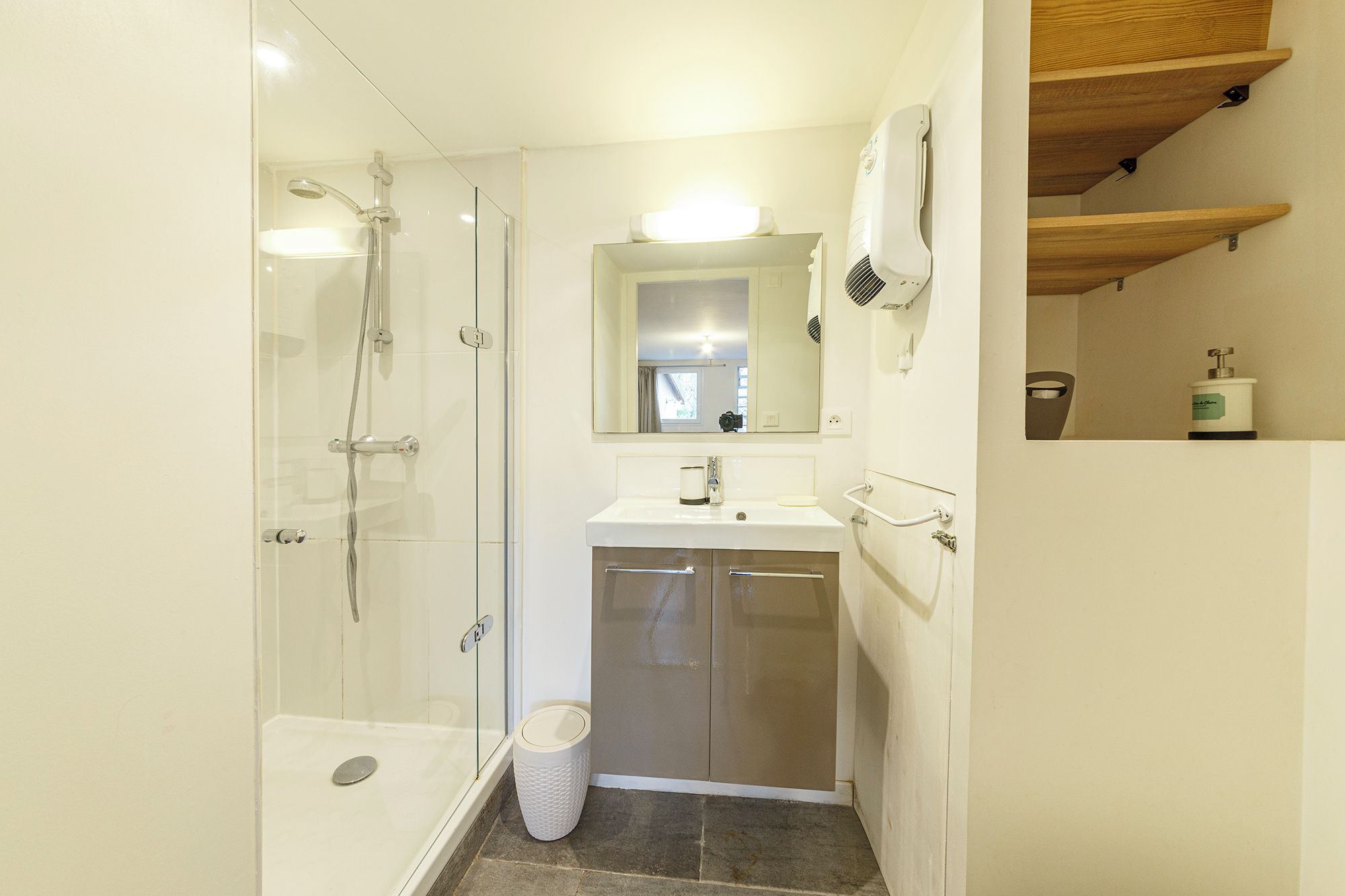 A compact bathroom with a glass-enclosed shower, a sink with a mirror above, and a trash bin.