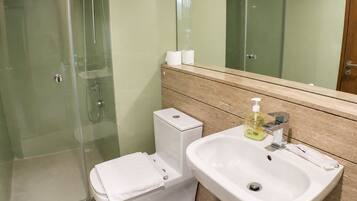 A bathroom with a glass shower enclosure, a toilet, and a sink with a soap dispenser.