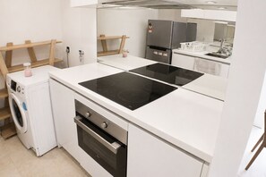 Une cuisine compacte équipée d’un lave-linge, d’un four et d’une plaque de cuisson à induction à deux foyers.