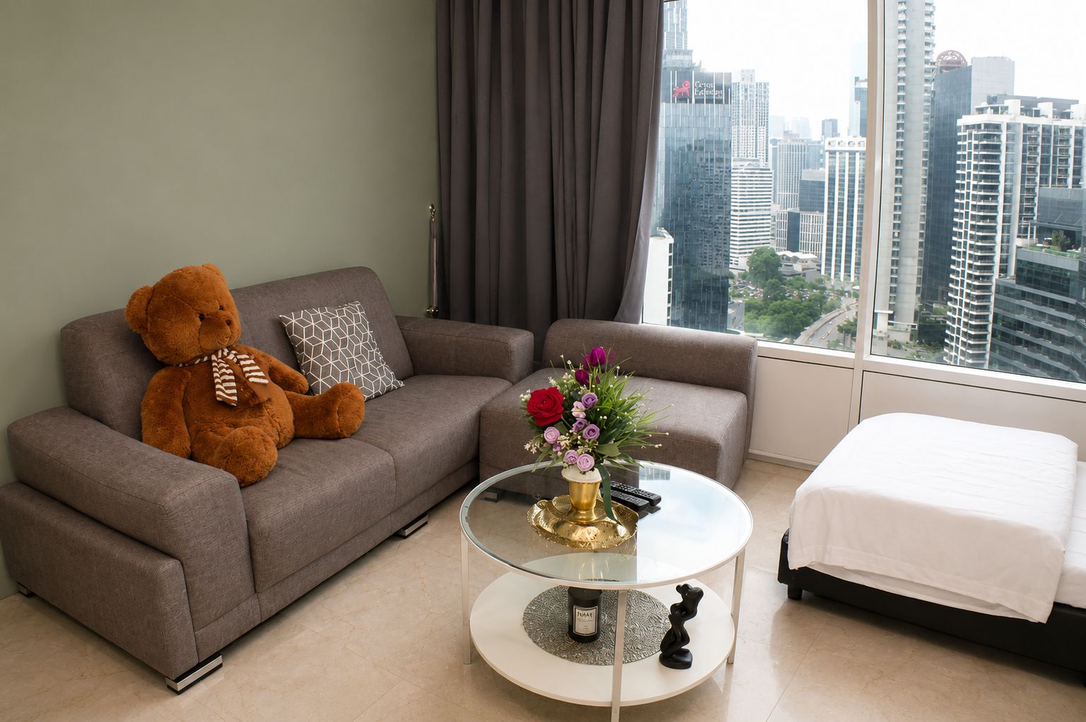 Ein modernes Wohnzimmer mit einer Couch, einem Glastisch, einem Bett und einem großen Fenster mit Blick auf die Stadt.