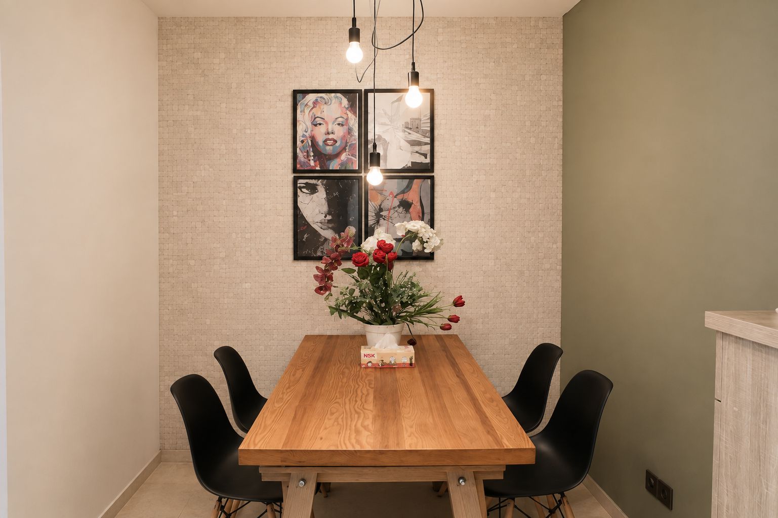 Un coin repas avec une table en bois, des chaises noires, un vase de fleurs et des œuvres d’art encadrées accrochées au mur.