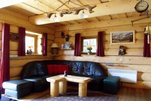 A log cabin interior with a black leather sofa, wooden tables, and a mounted clock. - Holiday home in Carinthia with 1 bedroom (Patergassen)