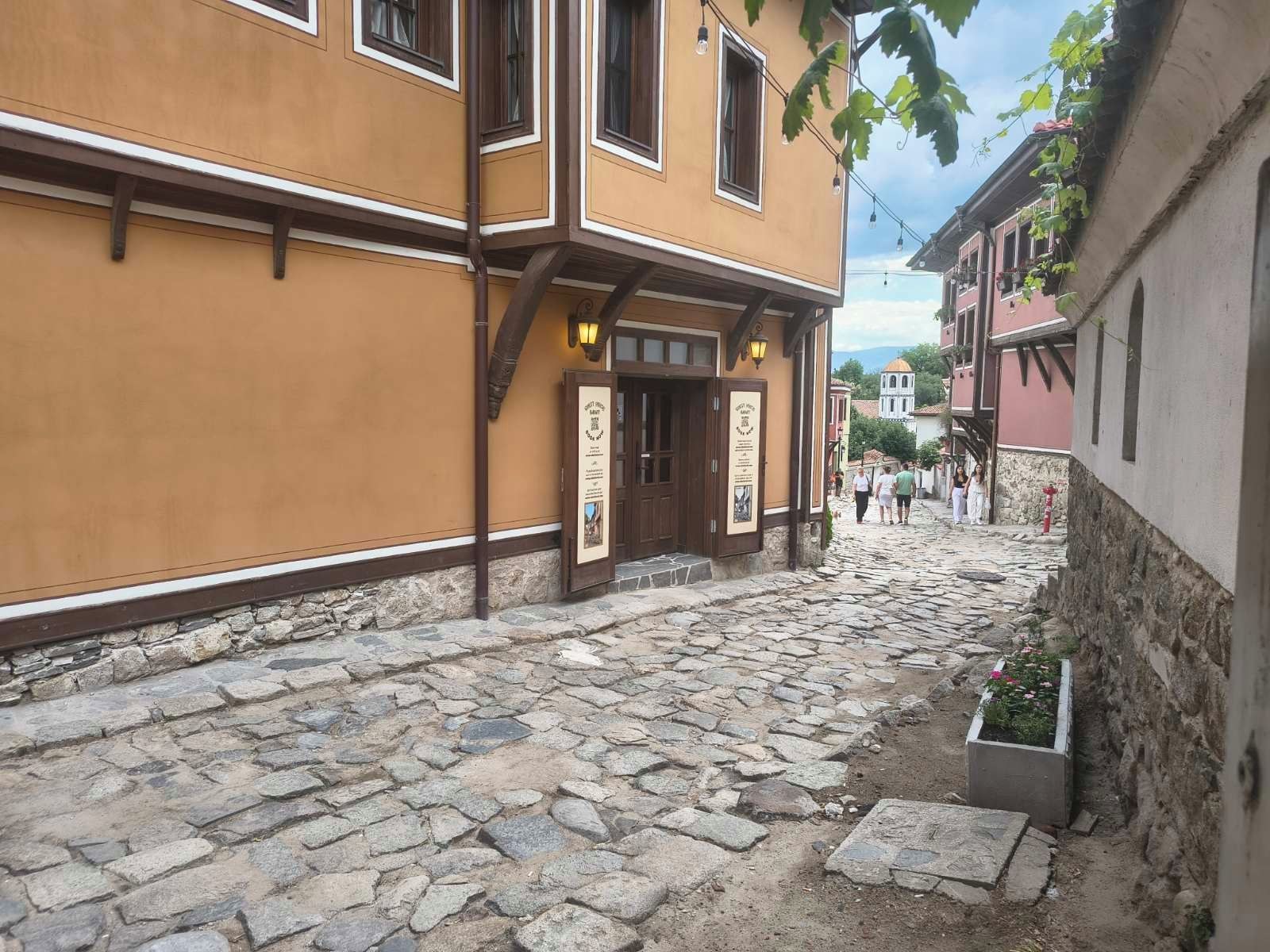 A cobblestone street with a building featuring a wooden door and a signboard.