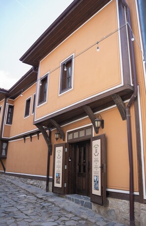 A traditional building with a stone-paved entrance, wooden beams, and two signs advertising a guest house. - Delightful 7-bedroom house with AC in vibrant Plovdiv (Plovdiv)