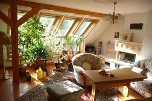 A cozy living room with a high ceiling, wooden beams, a fireplace, and a variety of plants. - Holiday apartment in Dittmannsdorf with sauna (Dittmannsdorf)