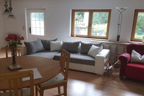 Un salon avec un canapé, un fauteuil rouge, une table à manger avec des chaises et un vase de fleurs.