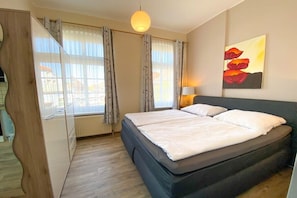 A bedroom with a bed, a window with curtains, a wall-mounted lamp, and a painting. - Guesthouse at the museum harbor (Carolinensiel)